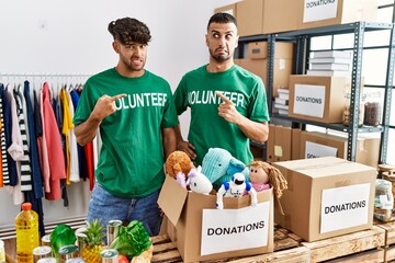 Poster - Young gay couple wearing volunteer t shirt at donations stand pointing aside worried and nervous with forefinger, concerned and surprised expression