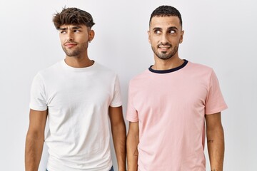 Wall Mural - Young gay couple standing over isolated background smiling looking to the side and staring away thinking.