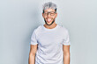 Young hispanic man with modern dyed hair wearing white t shirt and glasses sticking tongue out happy with funny expression. emotion concept.