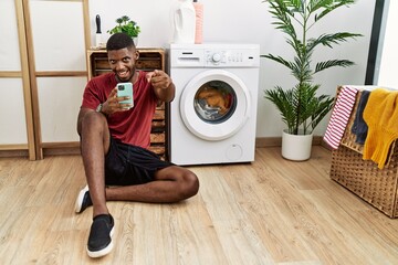 Canvas Print - Young african american man using smartphone waiting for washing machine pointing fingers to camera with happy and funny face. good energy and vibes.