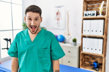 Poster - Young physiotherapist man working at pain recovery clinic afraid and shocked with surprise and amazed expression, fear and excited face.