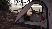 Brunette Girl With Braid Lies In Small Camp Tent On Manless Wild Beach Looking At Waves In Sea, Under Cloudy Sky On Gloomy Day In Vietnam