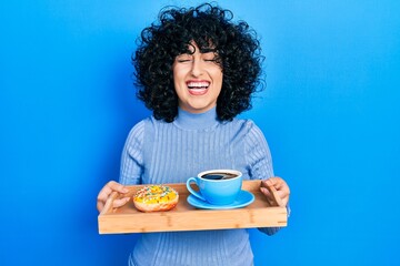 Sticker - Young middle east woman holding tray with doughnut and cup of coffee smiling and laughing hard out loud because funny crazy joke.