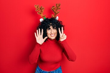 Poster - Young middle east woman wearing cute christmas reindeer horns showing and pointing up with fingers number seven while smiling confident and happy.