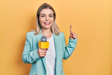 Beautiful caucasian woman holding reporter microphone smiling with an idea or question pointing finger with happy face, number one