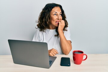 Poster - Beautiful middle age woman working at the office using computer laptop looking stressed and nervous with hands on mouth biting nails. anxiety problem.