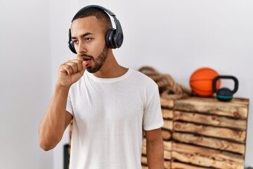 African american man listening to music using headphones at the gym feeling unwell and coughing as symptom for cold or bronchitis. health care concept.