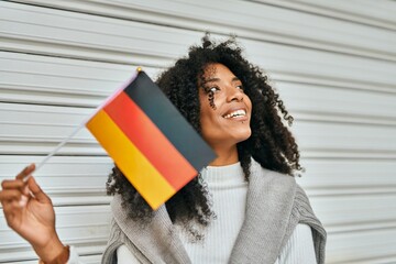 Wall Mural - Young african american woman smiling happy holding Germany flag at the city.