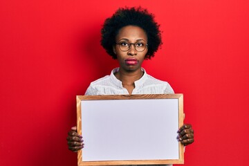 Sticker - Young african american woman holding empty white chalkboard relaxed with serious expression on face. simple and natural looking at the camera.