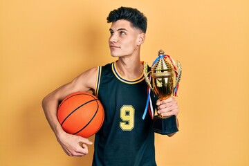 Canvas Print - Young hispanic man wearing basketball uniform holding ball and prize smiling looking to the side and staring away thinking.