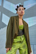 © wayhome.studio  - Self confident fashionable teenage girl dressed in green jacket and jeans has funny hairstyle poses against grey wall in public place has serious expression. Youth fashion and style concept.