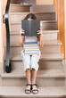 A girl on the stairs is reading a book. Several books lie on her lap.