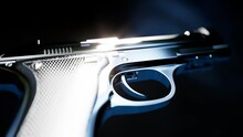 Elegant shiny pistol on dark background. Gun in harsh light.