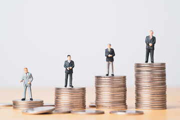 Different miniature businessman standing on different height coins stacking , Inequality income and salary in each position in company concept.