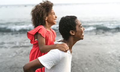 Wall Mural - Happy Afro mother and daughter having fun on the beach during vacations - Lovely family lifestyle concept