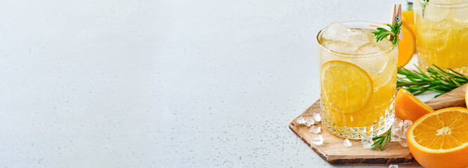 Orange juice or cocktail with rosemary and orange with ice in glass, cold summer lemonade on light gray slate, stone or concrete background. Beach concept with deep sun shadow. Top view.