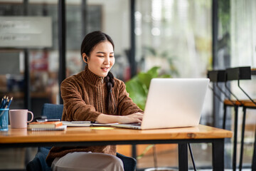 Young attractive university student using a laptop computer, studying online at home. Cheerful caucasian asian woman writes notes, planning working process, sitting at home. Exam preparation.