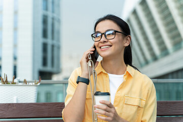 Waist up of young overjoyed woman having phone conversation and smiling while drinking coffee. Technologies and people concept. Stock photo