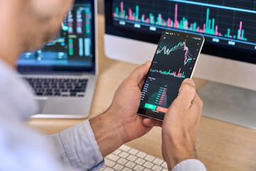Crypto trader investor broker using smartphone app analyzing financial data stock market price on cell phone, checking online trading platform application, buying cryptocurrency, over shoulder view.
