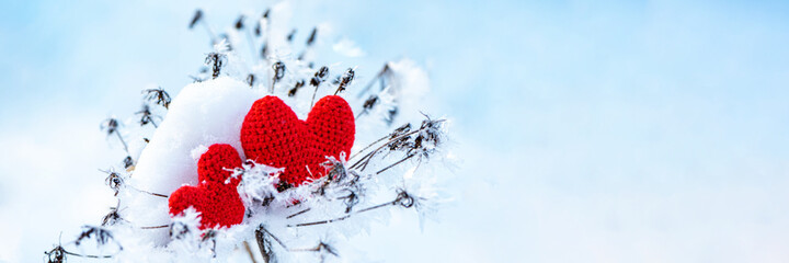 Red knitted hearts lying on white snow and twigs on light blue background as symbolic postcard for Valentines day celebration