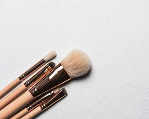 beige makeup brushes lying diagonally on a white table