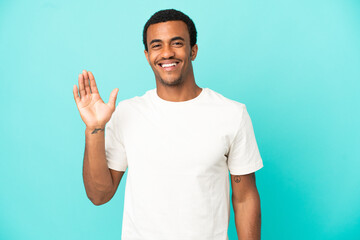 Wall Mural - African American handsome man on isolated blue background saluting with hand with happy expression