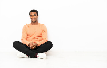 Wall Mural - African American man sitting on the floor over isolated copyspace background posing with arms at hip and smiling