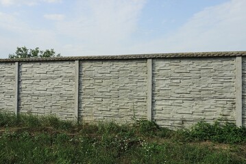 Canvas Print - part of a long gray white concrete fence wall on a rural street in green grass