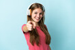 © luismolinero - Young caucasian woman isolated on blue background listening music and pointing to the front