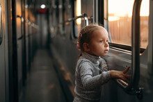 Toddler Child Looking Though Train Window On Sunset, Bright Sunlight, Atmospheric Travel By Railway With Kids. Girl Happy Exploring The Way In Evening. Exciting Family Trip