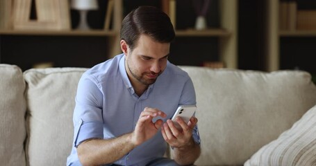 Wall Mural - smartphone user. millennial man sit on couch focused on phone screen play mobile game online write m
