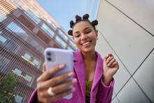 Stylish Lady With Hairstyle Dressed In Fashionable Pink Jacket Takes Selfie On Mobile Phone For Social Networks Poses Against Blurred City Buildings Smiles Happily Enjoys Free Time Streams Video