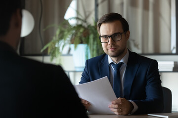 Poster - Smiling hr manager sit at desk opposite male candidate on vacant post study cv hold job interview. Young man recruiter in formal attire glasses ask applicant questions about professional experience