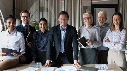 Canvas Print - Professional leader and staff. Smiling young male ceo boss executive posing ahead of successful international work group at office boardroom. Portrait of happy diverse business partners look at camera