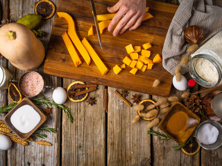 Lots of ingredients for making a classic American pumpkin pie. decor. A cook in a dark uniform slices fresh orange pumpkin. A high angle view. Wooden texture.