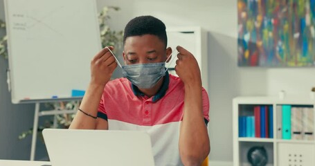 Wall Mural - A young boy with dark complexion with a protective mask on face works on an ambitious project, an office worker looks into the camera, removes the mask from face smiles