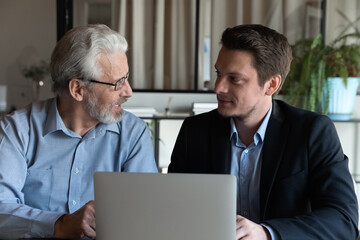 Poster - Two diverse male colleagues sit at office desk by laptop talk discuss business project create new idea strategy. Focused young hr manager listen to senior man candidate for position at job interview