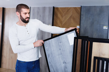 Portrait of cheerful positive man choosing wood laminated flooring in shop