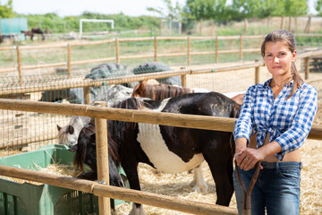 Happy confident young woman horses breeder standing near fencing of stable outdoors