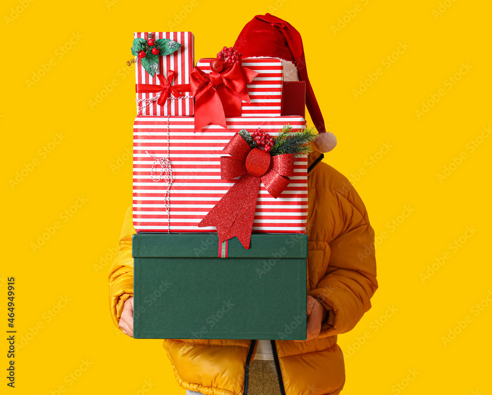 Man in Santa hat holding Christmas gift boxes on yellow background