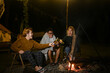 © Prathankarnpap - Group of young people sitting near campfire and drinking beer at night together.