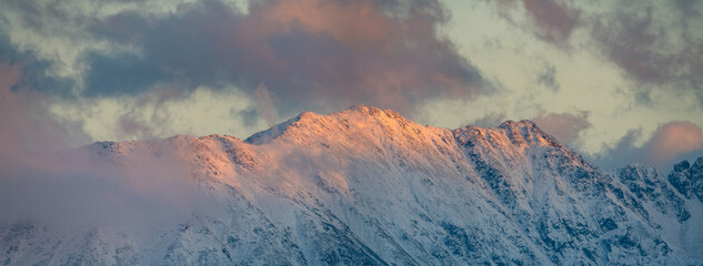 Wall Mural - Panorama of snow-covered mountain peaks in the light of the setting sun