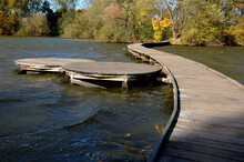 Floating Walkway Made Of Wooden Planks. Narrow Curved Paths On Stilts Driven Into The Bottom, Above The Lake Water. Has No Railings. More Design Walkway Made Of Individual Circular Boards. Autumn
