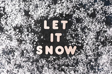 Text Let It Snow On Dark Background With Snowflakes, Winter Time. Flat Lay
