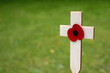 Red puppy flower placed on the small wooden cross in the green grass. Poppy remembrance day cross in a field