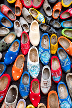 Background Of Popular Souvenirs - Old Wooden Dutch Shoes - Klomps. A Lot Of Colorful Old Clomps Against The Background Of A Wooden Wall. Traditions Of Holland.