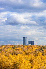 Wall Mural - dark gray rainy clouds in blue sky over lush yellow forest and high-rise buildings on sunny autumn day before rain