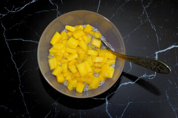 Wall Mural - chia pudding with coconut milk and mango slices and a spoon stands on a black marble table. top view. light dessert gluten-free, lactose-free