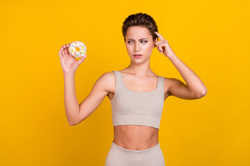 Wall Mural - Photo of unsure doubtful lady hold doughnut decide diet wear grey top isolated yellow color background