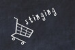 Chalk drawing of shopping cart and word stinging on black chalboard. Concept of globalization and mass consuming